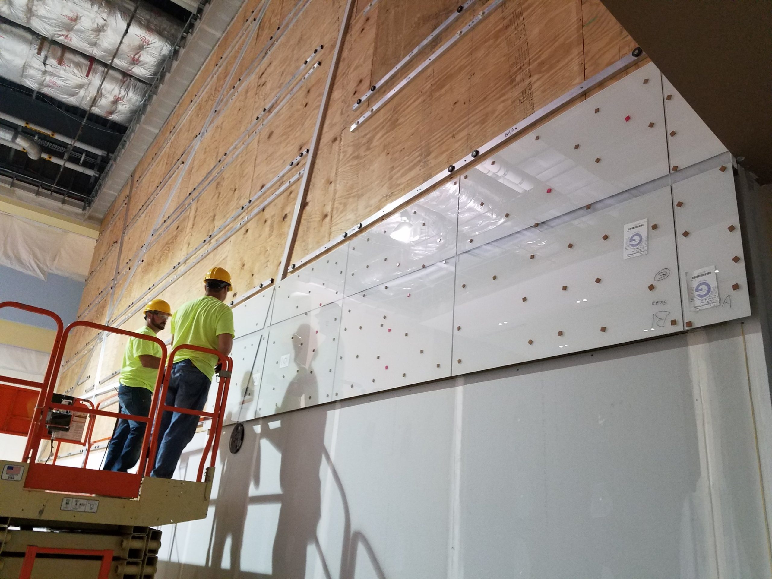 First row of back painted glass going up Crew on a scissor lift setting the first rows of back painted glass panels on a Columbus Convention Center node wall, plywood and channels visible above