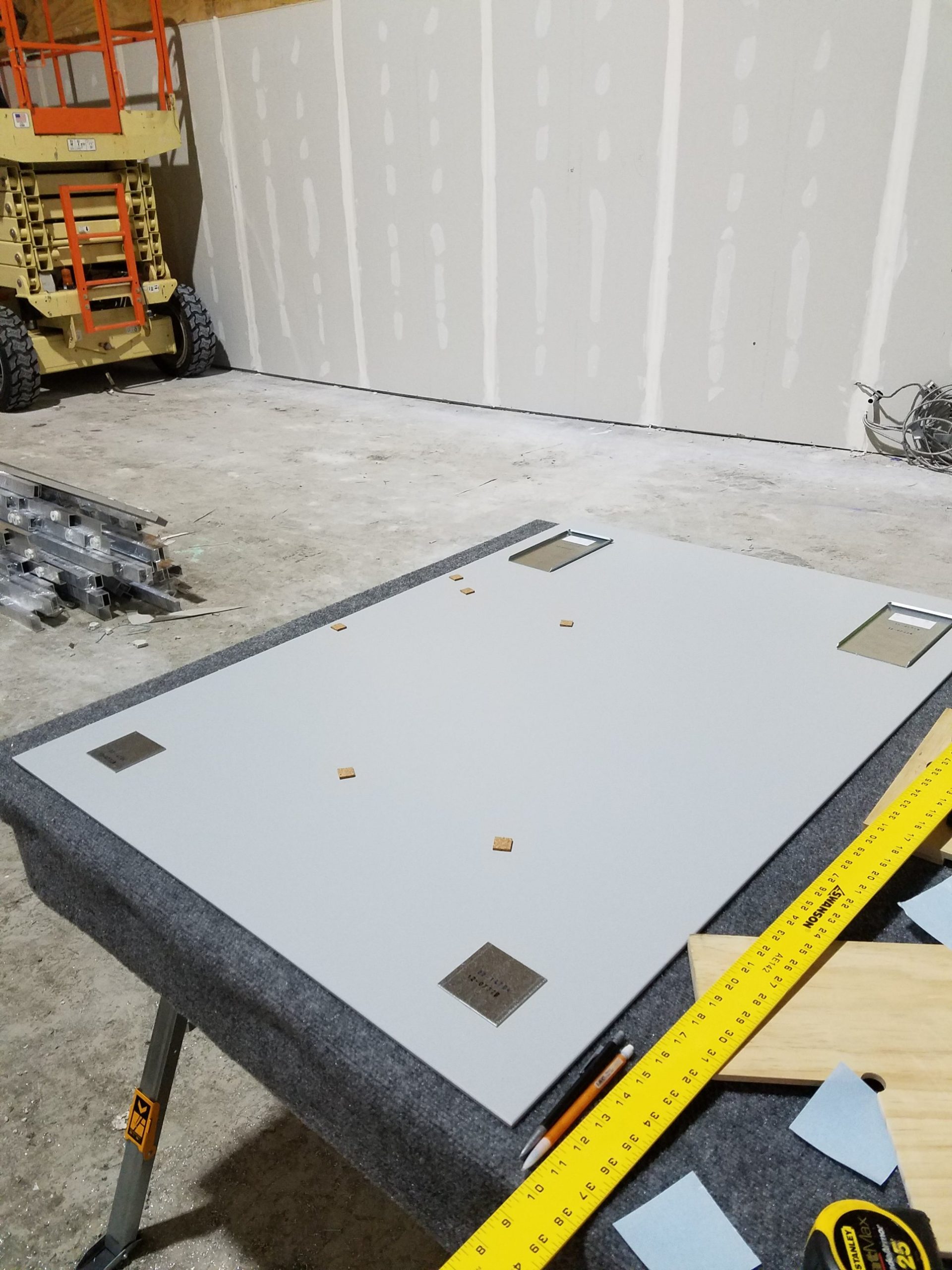 Node wall panel with brackets and pads Back painted glass panel on a shop table with four hanging brackets and cork pads located on the painted back before installation