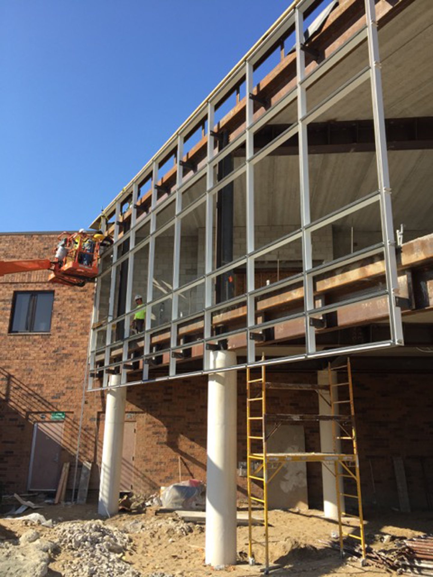 Novi High School fitness center under construction, curtain wall verticals anchored with clips to cantilevered structural steel, no sill wall